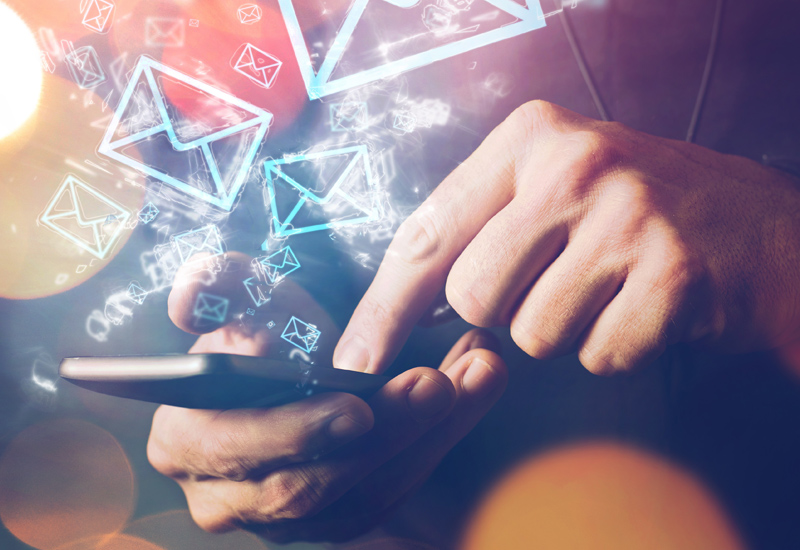 an image showing a person holding a phone on its side touching the screen with his finger with email icons flying out of the screen